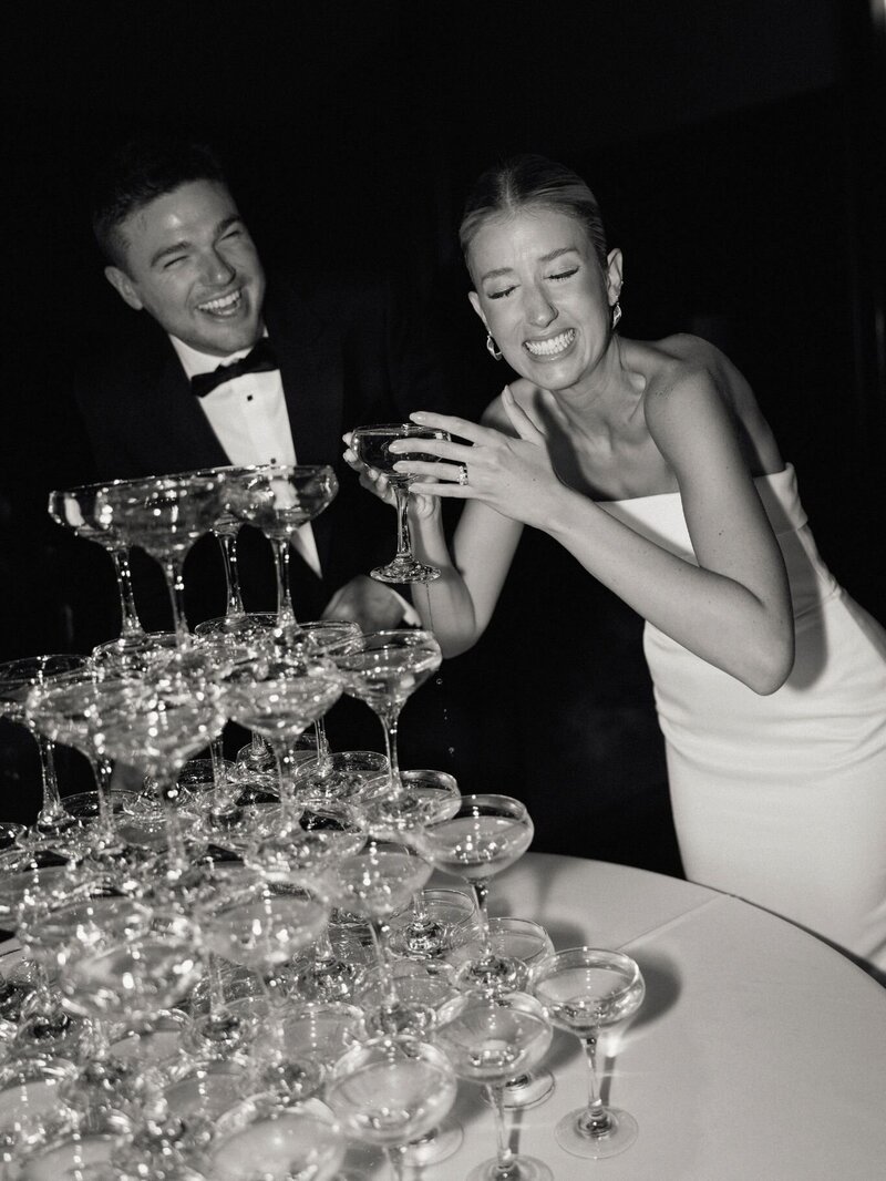 Bride and groom celebrate by pouring champagne into a glass tower during the wedding reception.