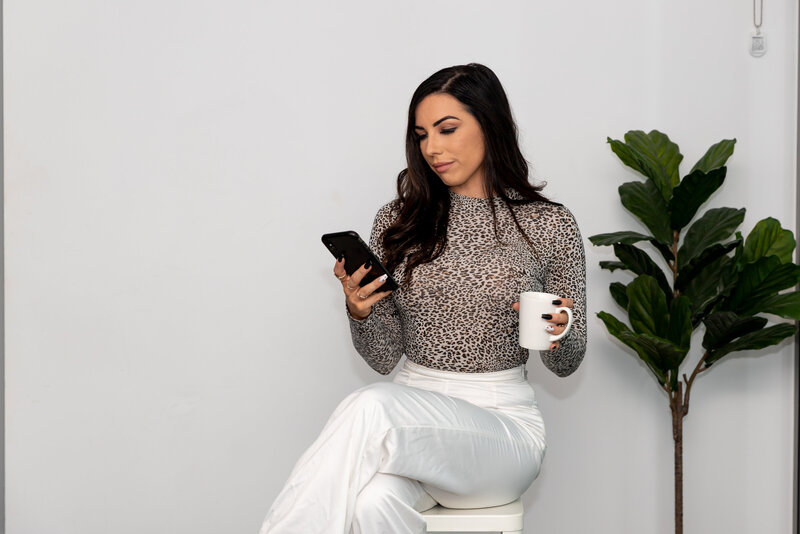 Woman hold a phone and a coffee cup sitting on a stool