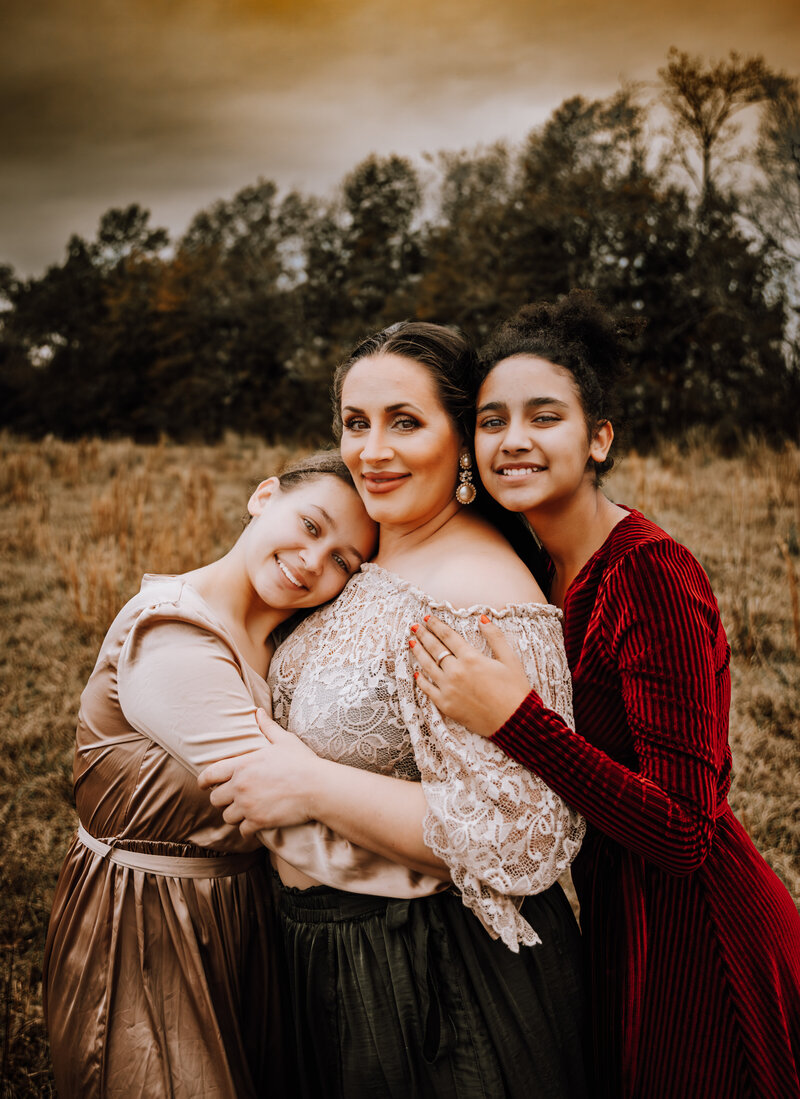 mom and daughters snuggling close outside during sunset for a family session