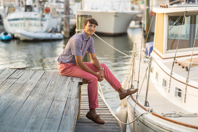 High School Senior boy wearing pink sitting on a dock by a boat