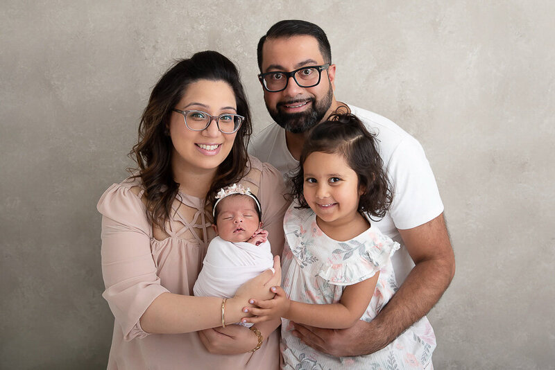 Family newborn photo of mom and dad with two daughters on a beige background for their newborn photos.
