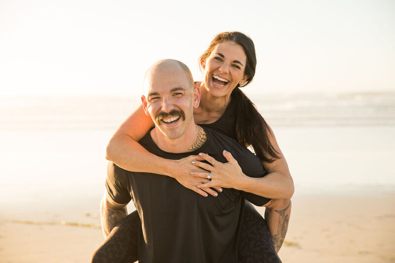 Jackie and Scott of Iron and Salt Fitness laughing piggyback on Marin County beach.