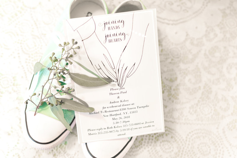 Wedding invitation and bouquet greenery on to of brides sage colored Converse sneakers