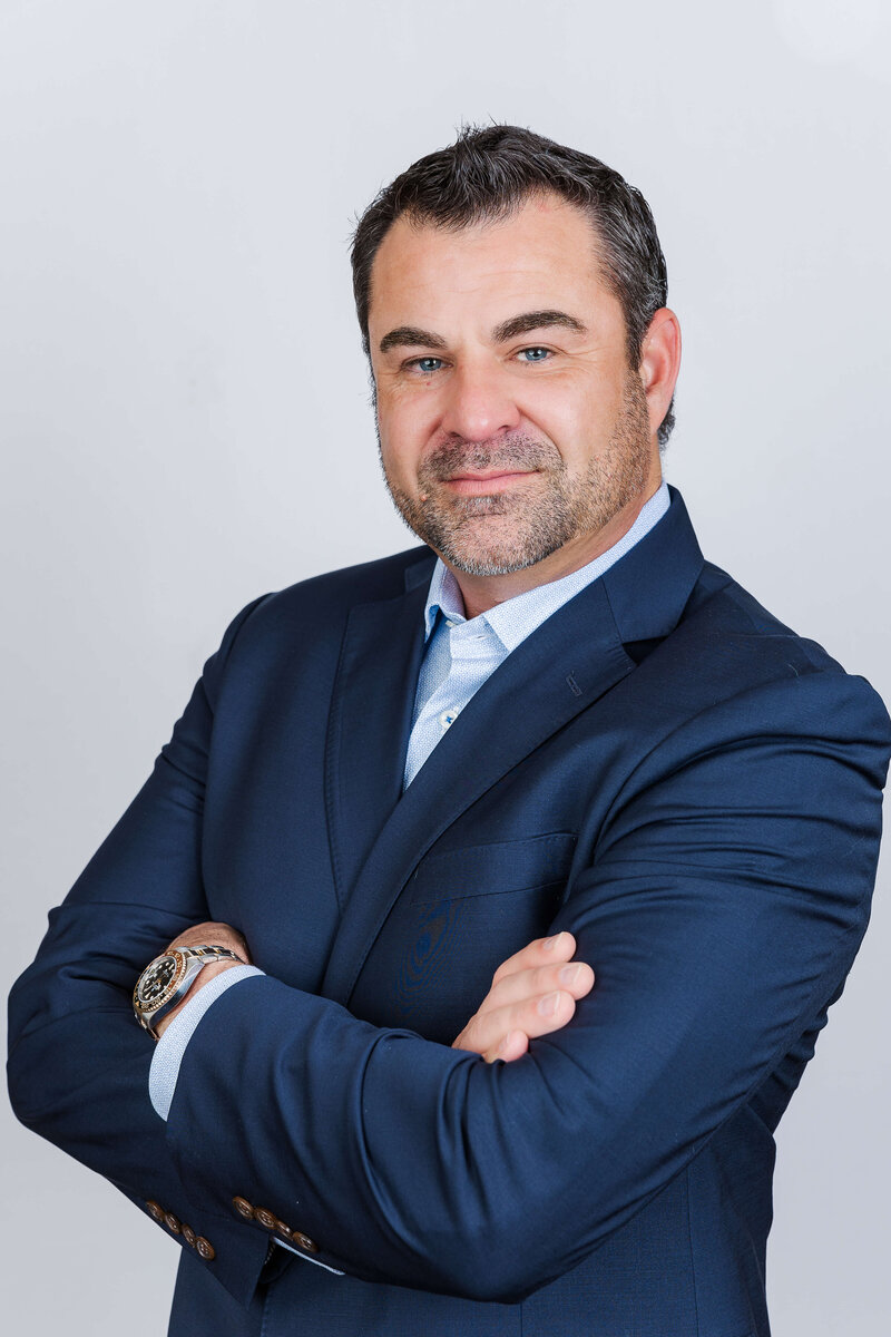 Headshot of man with arms folded in navy suit