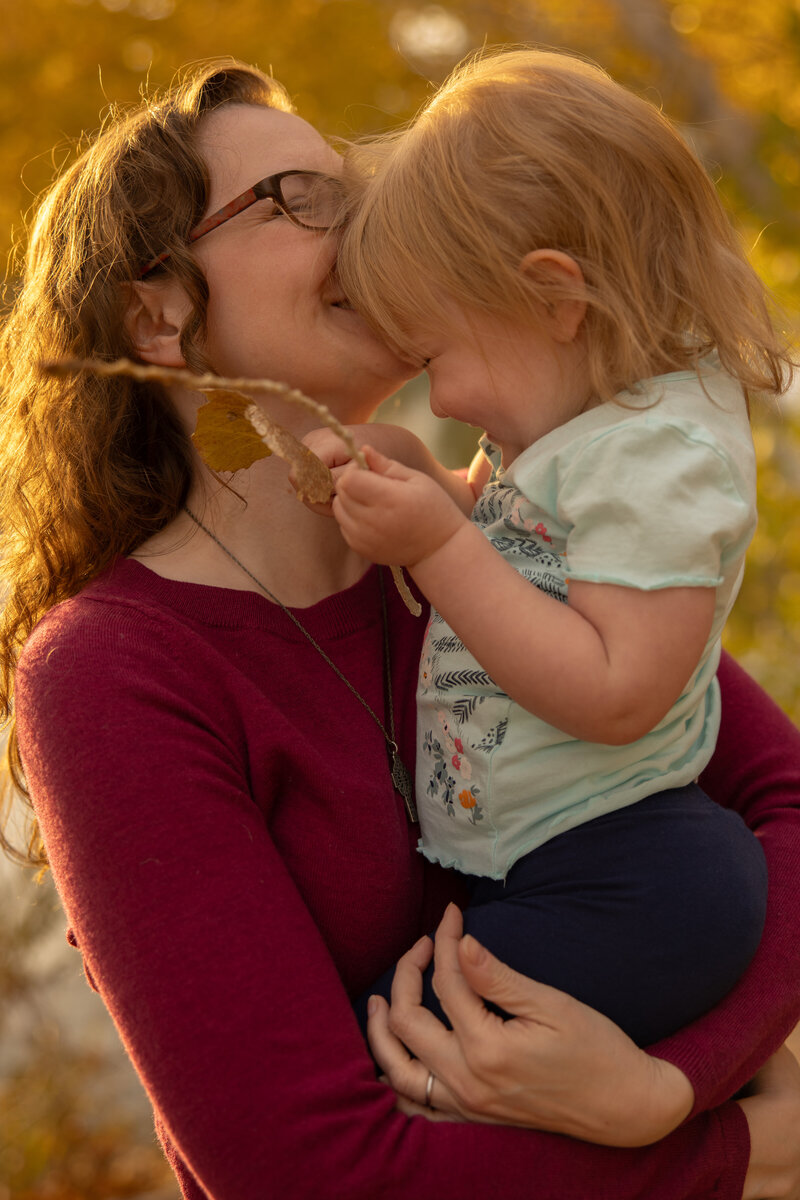 mom holding her toddler daughter and laughing about the sticks and leaves during their portrait session with las vegas photographer alexis dean