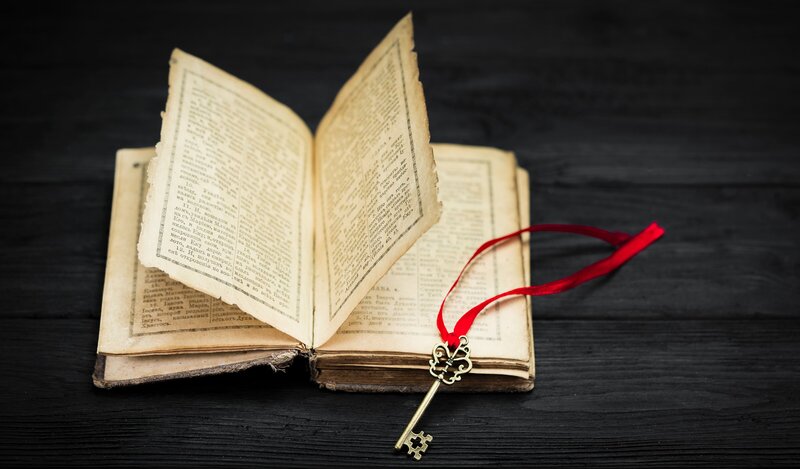 Biblia antigua abierta con una llave dorada y cinta roja, simbolizando el acceso a sus mensajes codificados.