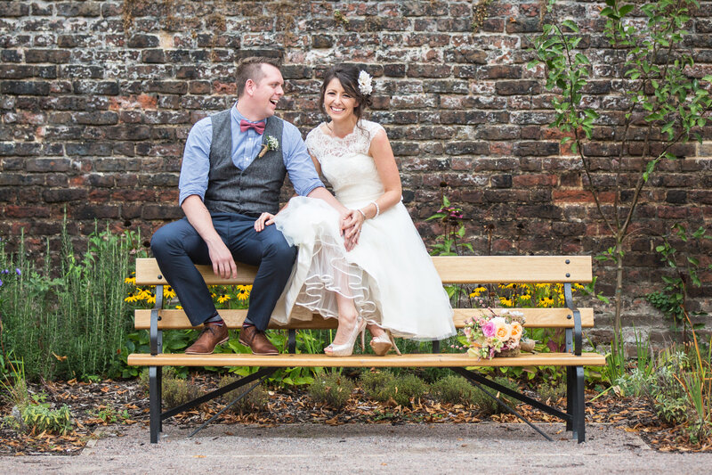 bride and groom laughing together on park bench