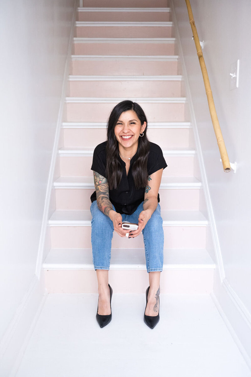 Karen sits at the bottom of a light pink and white staircase holding her phone with both hands