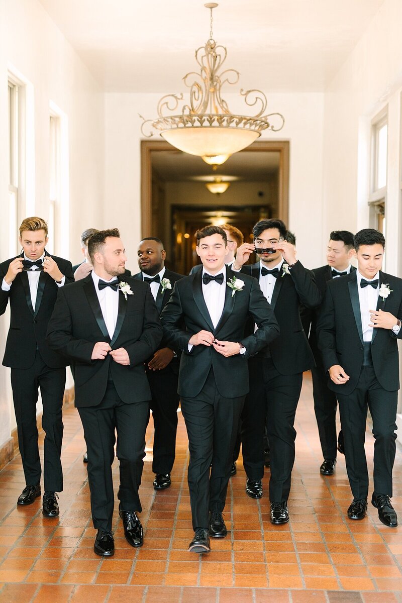 Groom and groomsmen in black tuxes walking down the hallways together buttoning jackets in Jeune Perche, California.