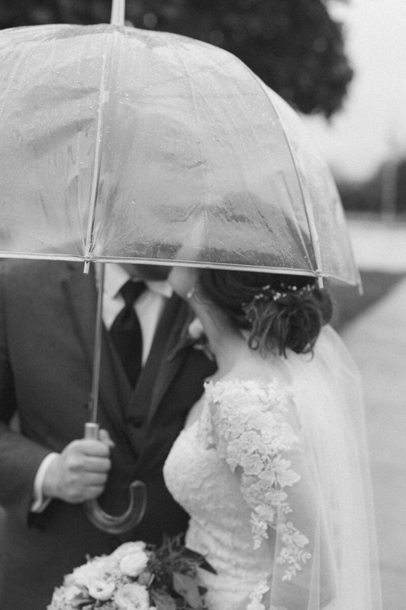 black and white image bride and groom kissing under umbrella