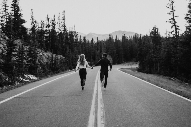 a couple holding hands running down the street together during their engagement photos