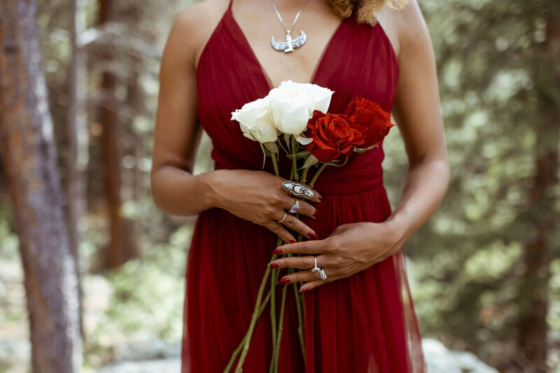woman with a red dress standing in the forest with a white and red roses bouquet
