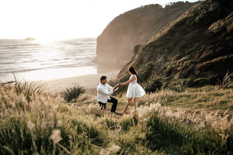 Wide landscape photo of a man down on his knee proposing to a woman with the clifftops and ocean in the background - Zanthe Vorsatz Photography