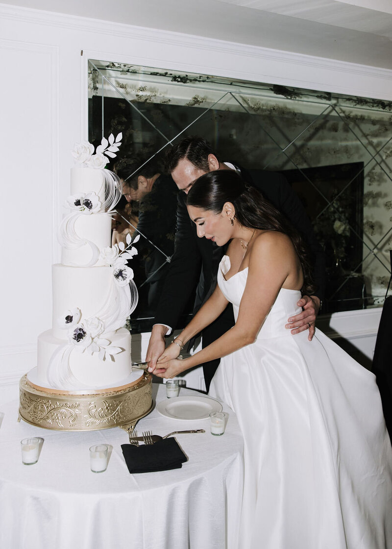 Cake artist posing with whie wedding cake and pink and peach sugar flowers