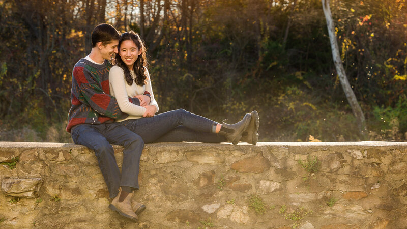 Couple sitting on a stone wall, snuggling and sharing a private moment at Valley Forge National Historical Park.