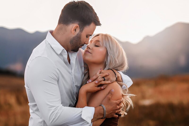 Dapper couple posing in each others arms in front of the Rocky mountains.