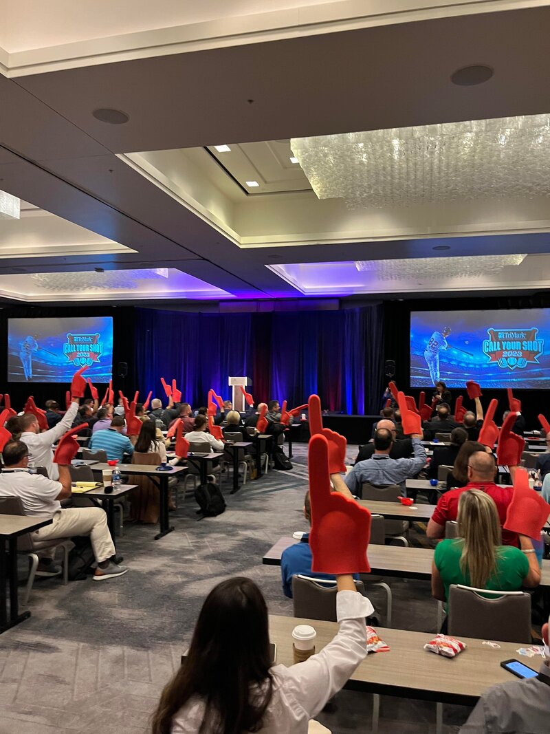 Wide shot of audience members who are holding foam  fingers  in the air as they welcome Brittany Hodak on the stage.