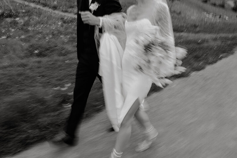 couple in wedding dress and suit walk by camera linking arms