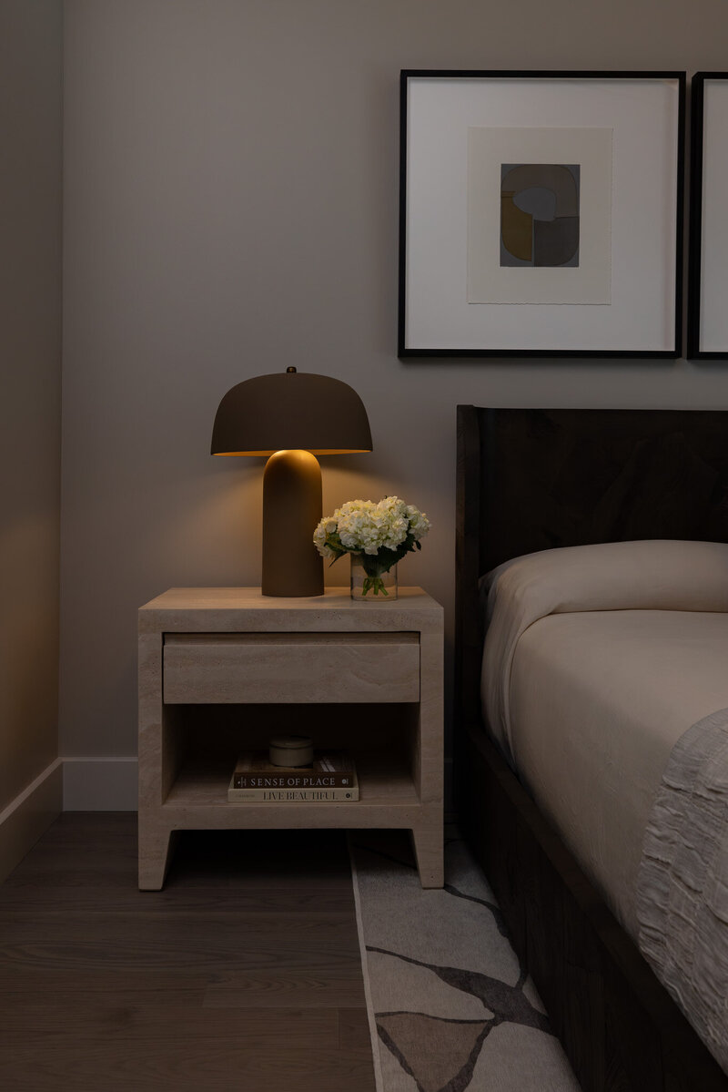 Close-up of a burlwood bed and travertine nightstand with a sculptural lamp and styled decor in the primary bedroom, designed by Sister Studio.