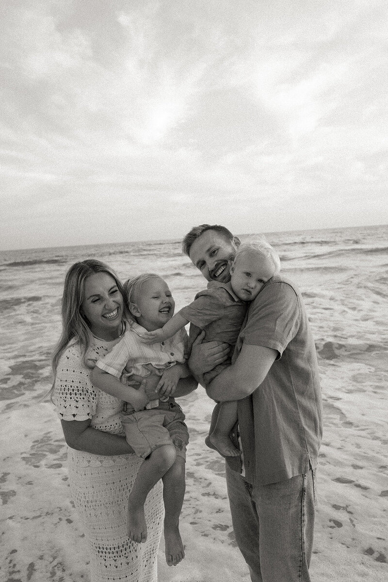family of 4 playfully laughing together at the beach 
