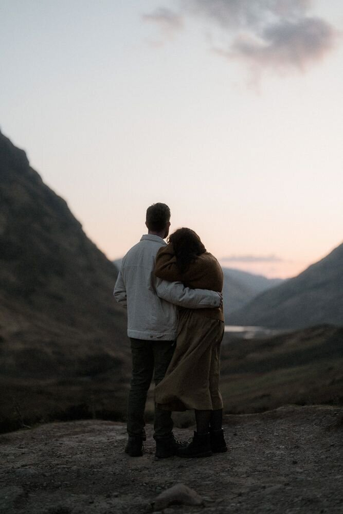Couple stand close together and admire the sunset after their photoshoot in Glencoe, Scotland