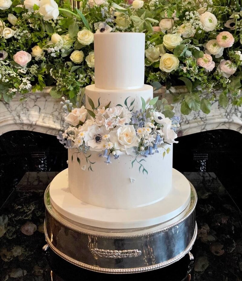 A two tier wedding cake with lots of sugar flowers covering the second tier