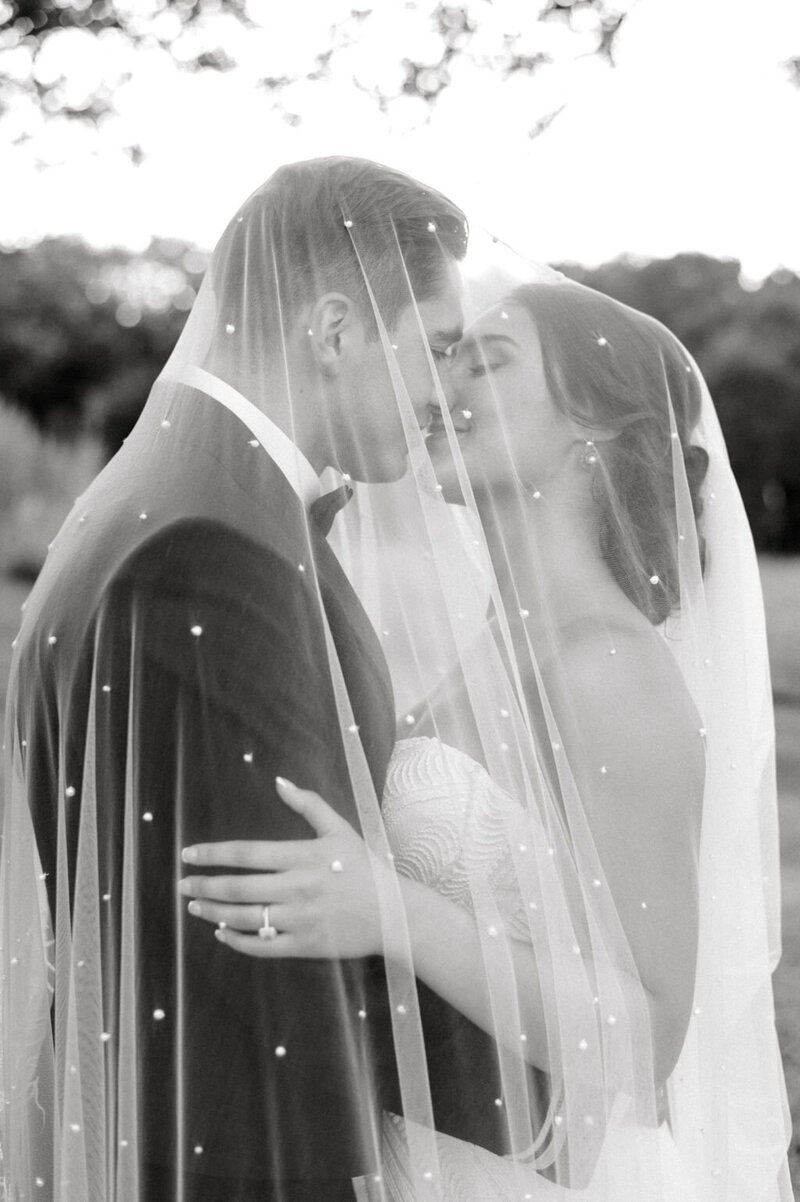 Black and white image of bride and groom kissing underneath veil