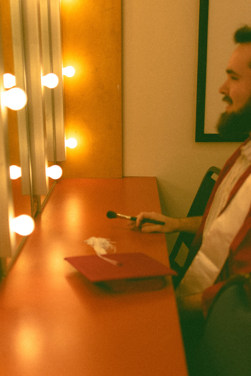 Graduating theater major sitting in front of a make up mirror.