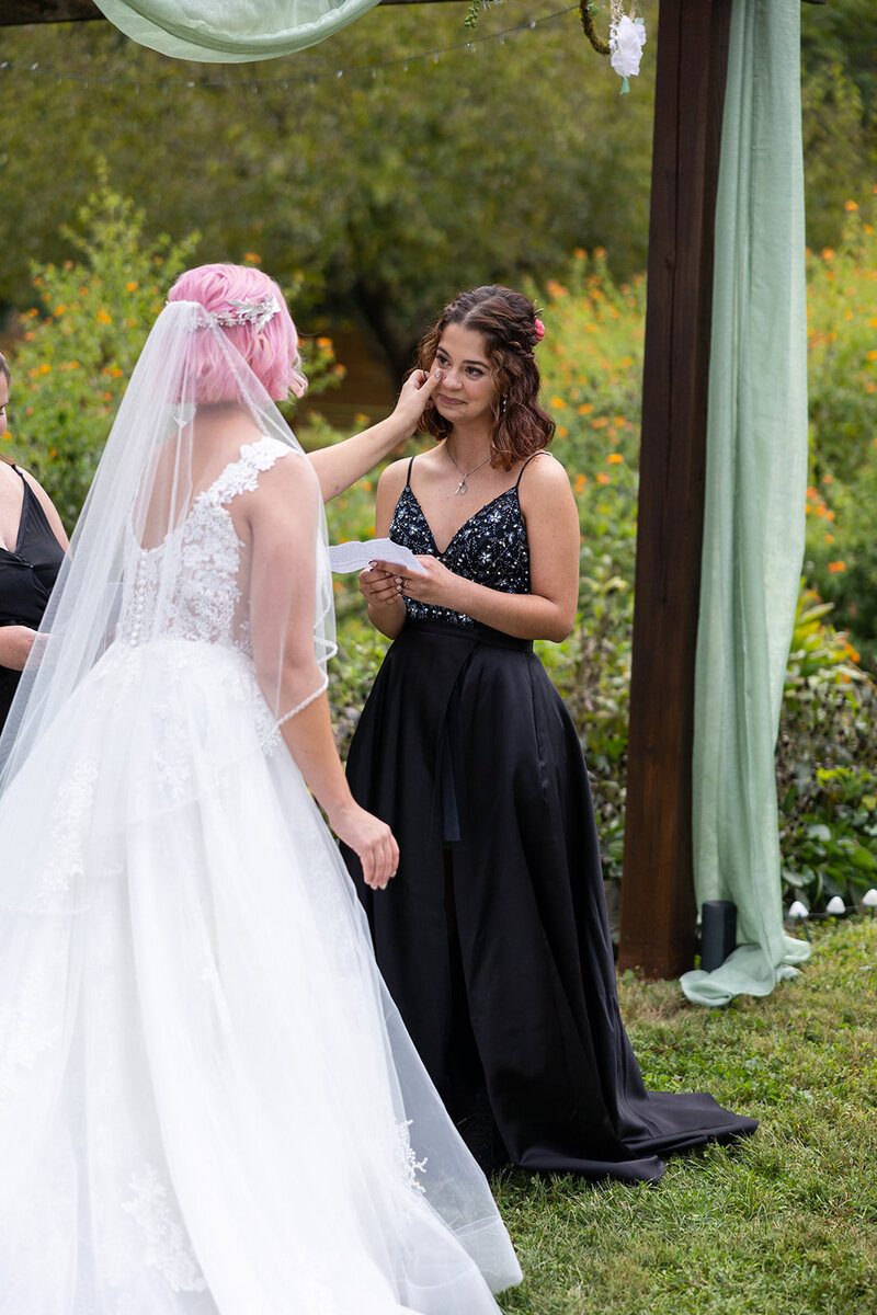 Bride in white princess dress wipes tears away from bride in black dress at their raleigh wedding
