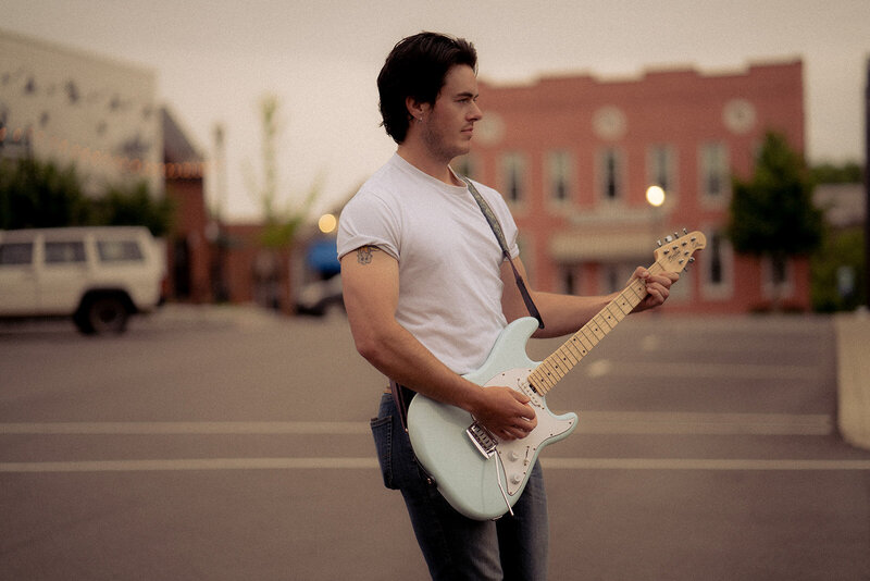 Rock musician poses in the streets of nashville with his electric guitar for an album cover.