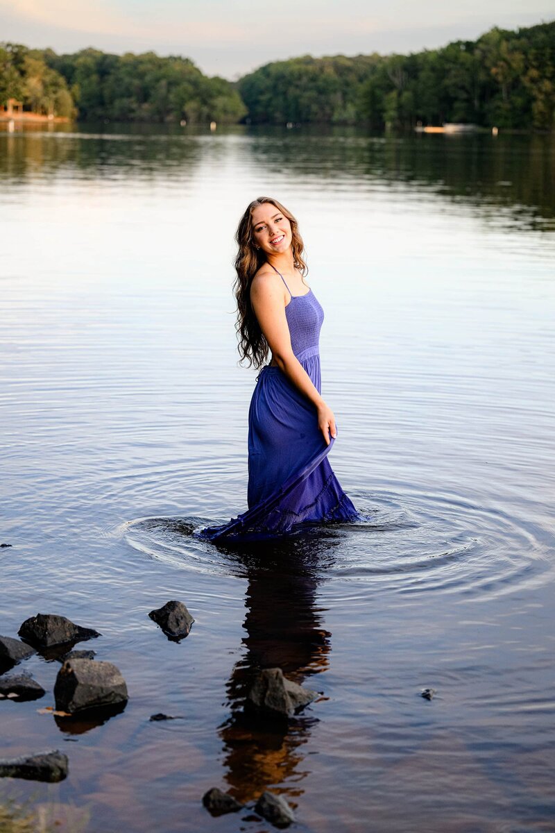 senior looks back over her shoulder durin gher senior photo session while standing in water