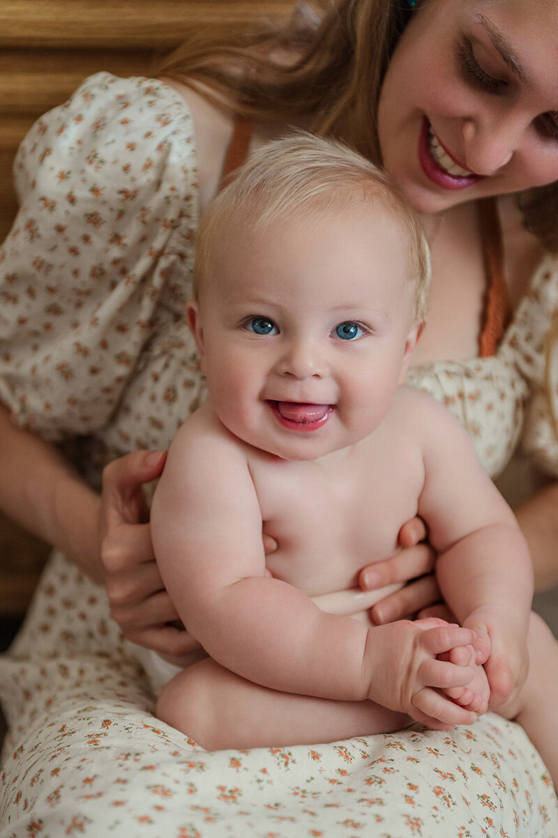 mother in a white and orange flowered dress holding her smiling baby on her lap by york pa photographer
