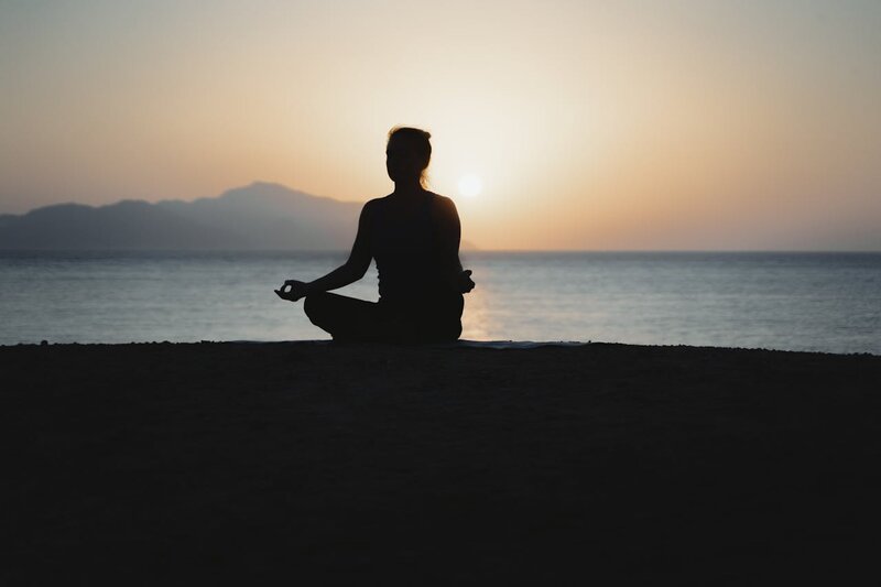 The silhouette of a woman meditating by a by a lake. 