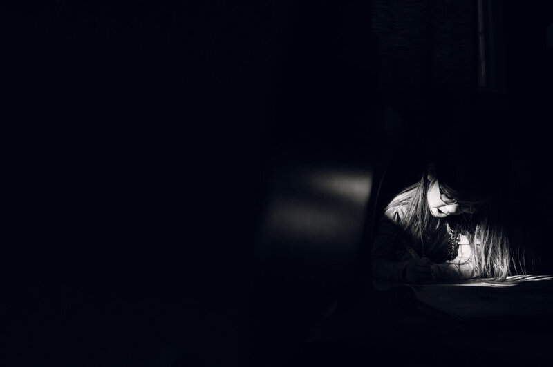 A black and white photo of a girl reading a book in the dark.