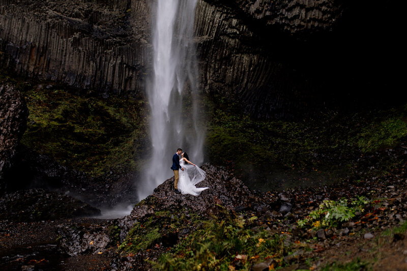 Couple sharing a kiss beneath a cascading waterfall, showcasing adventurous love with an Oregon Coast Elopement and Wedding Photographer.