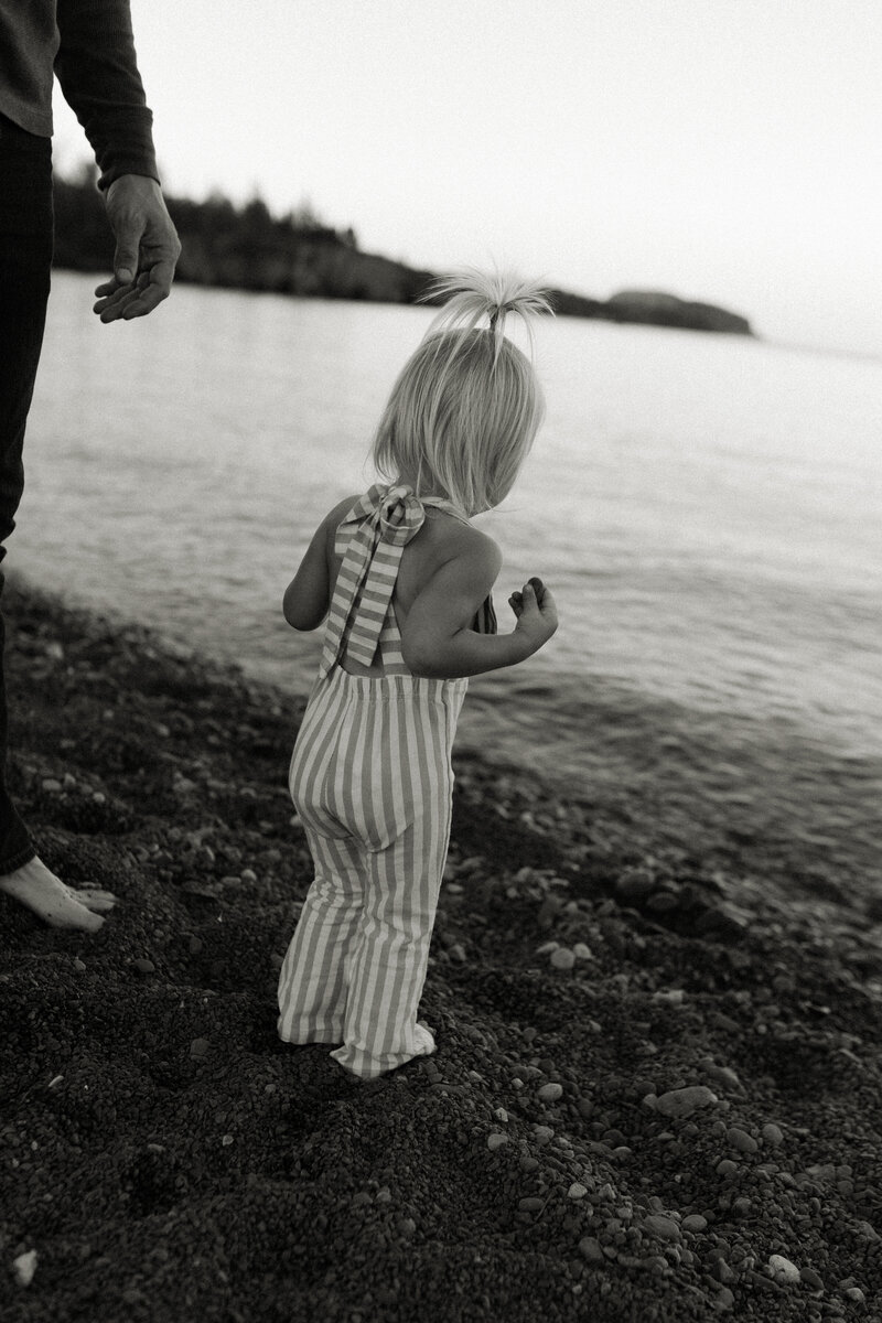 A toddler girl watches waves come to shore at Black Beach during a family session along the North Shore.