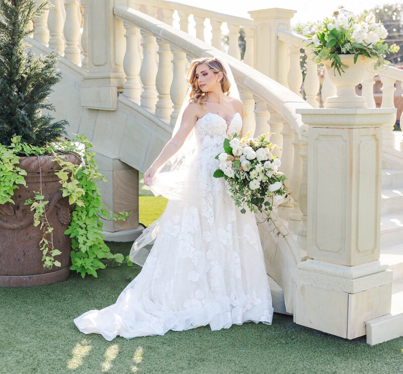 Discover the timeless beauty of this stunning bridal portrait, featuring a bride in a lace gown holding a lush bouquet. Captured at a luxurious garden venue, this image exudes elegance and romance, perfect for wedding inspiration.