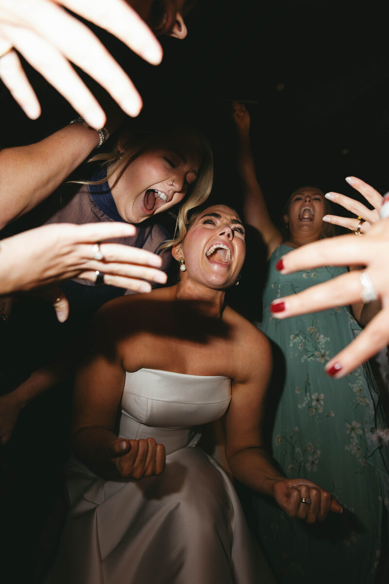 Bride laughing surrounded by friends during wedding reception, captured by Clar Barron Photo, luxury wedding photographer in Northwest Arkansas.
