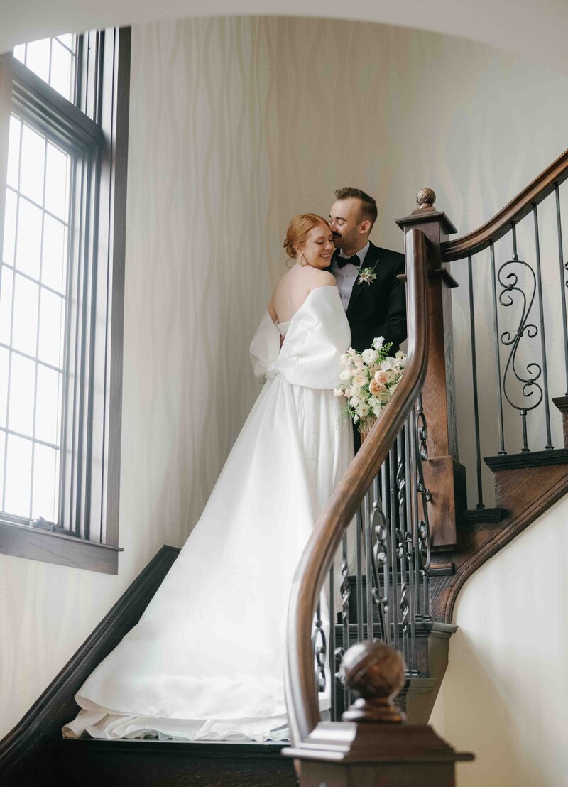 A couple snuggles on a curved staircase at their wedding at a old manor.
