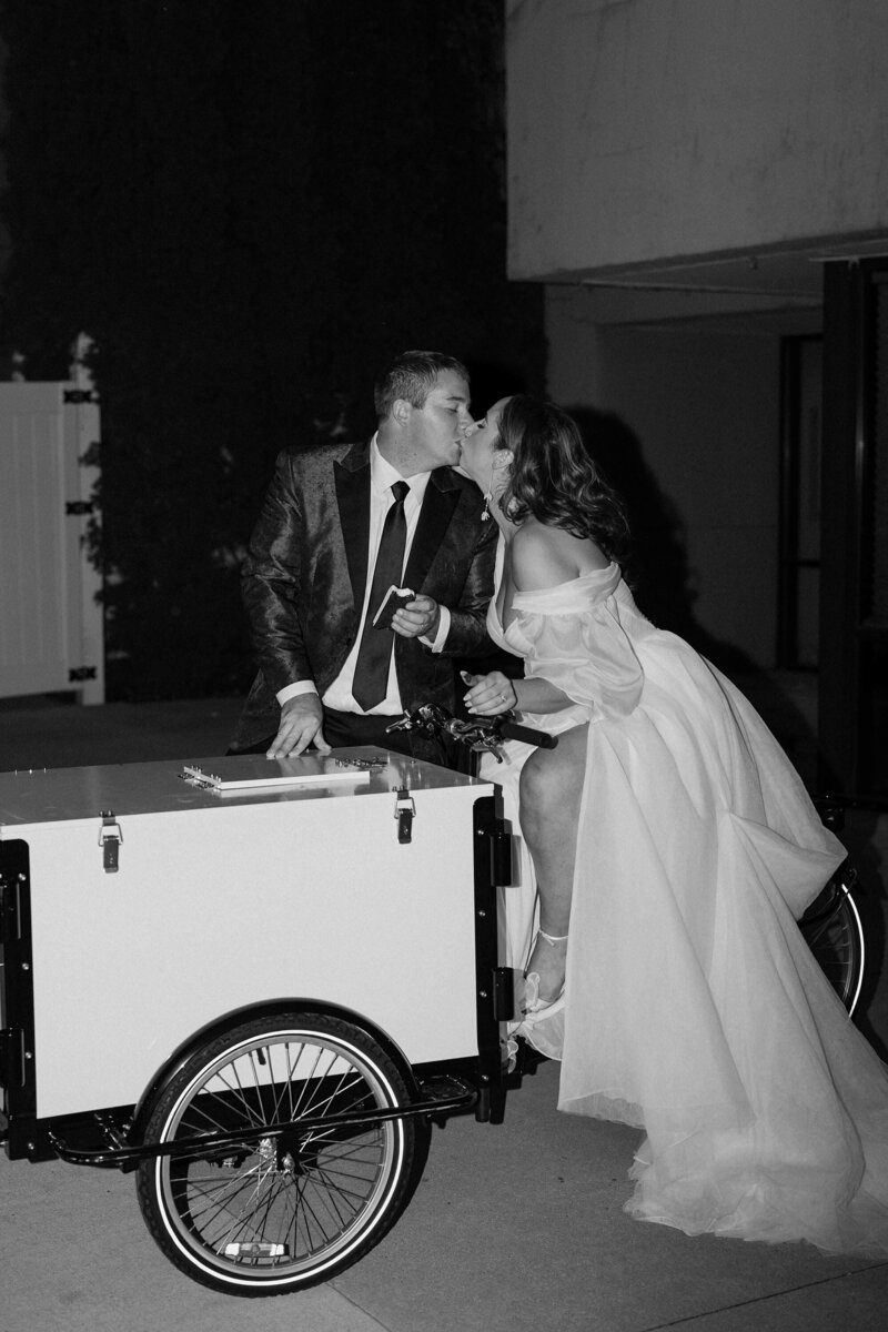 A newlywed couple kissing on an ice cream bike 