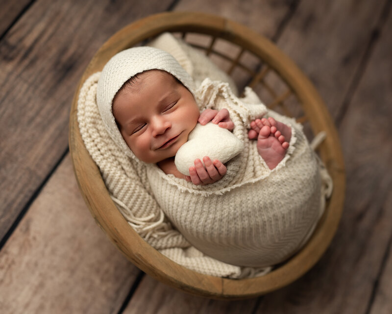 Sweet and simple—this smiling baby boy clutches a soft felt heart while wrapped in creamy textures and love.