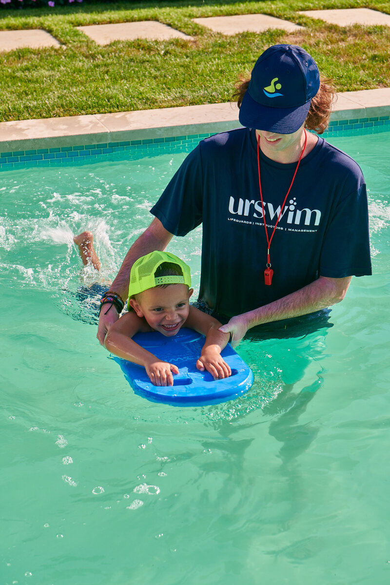 A lifeguard patiently guides a child in using a float board, promoting water safety through expert instruction
