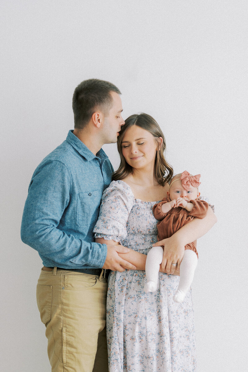 dad kissing mom on the head while she holds baby girl