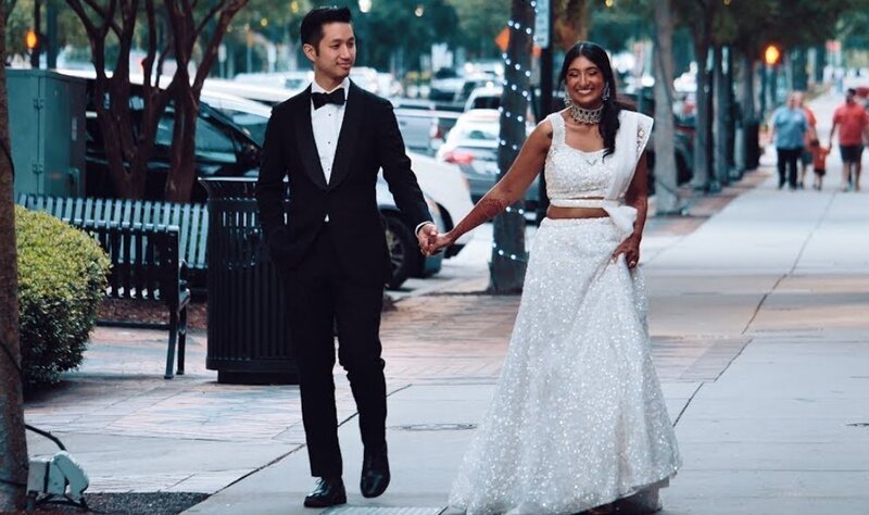 A newlywed couple holding hands and walking down a sidewalk 