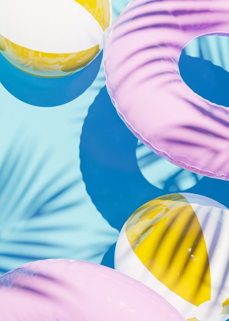 pink pool tubes and yellow beach balls floating on a crystal blue pool surface socialfizz