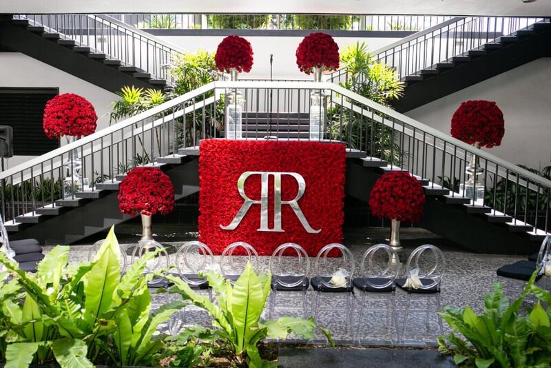 A staircase with a wall of red roses in front and two Rs in gold on it.