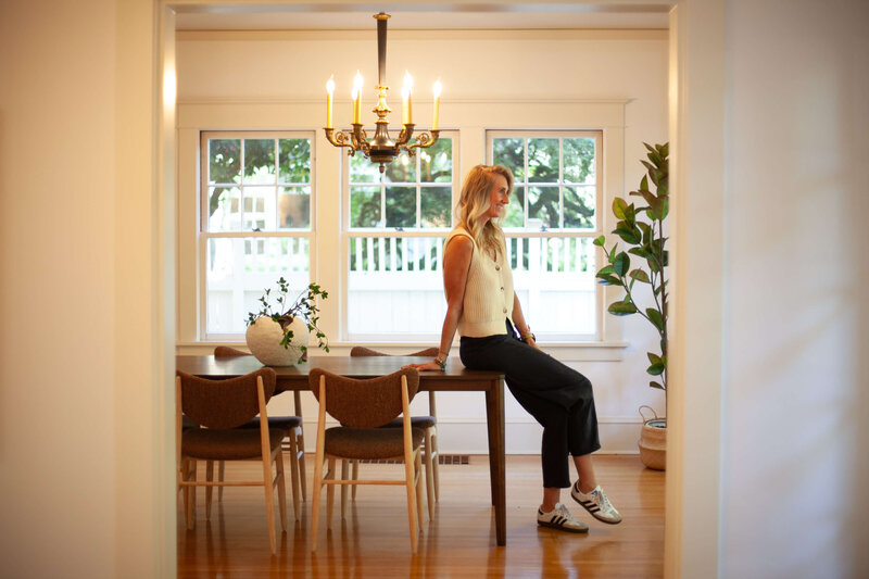 Stephanie, a relocation real estate agents sits on the edge of a table in a dining room.