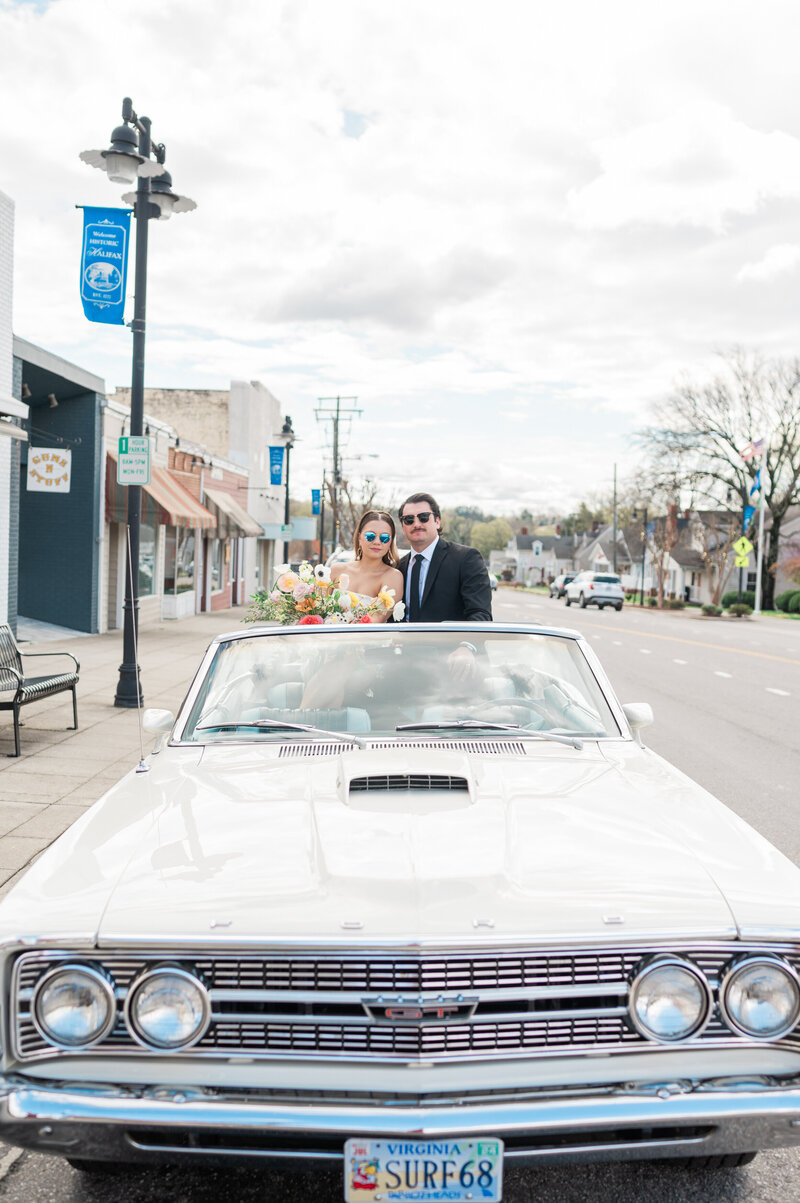 A newlywed couple sitting in a convertible with sunglasses on