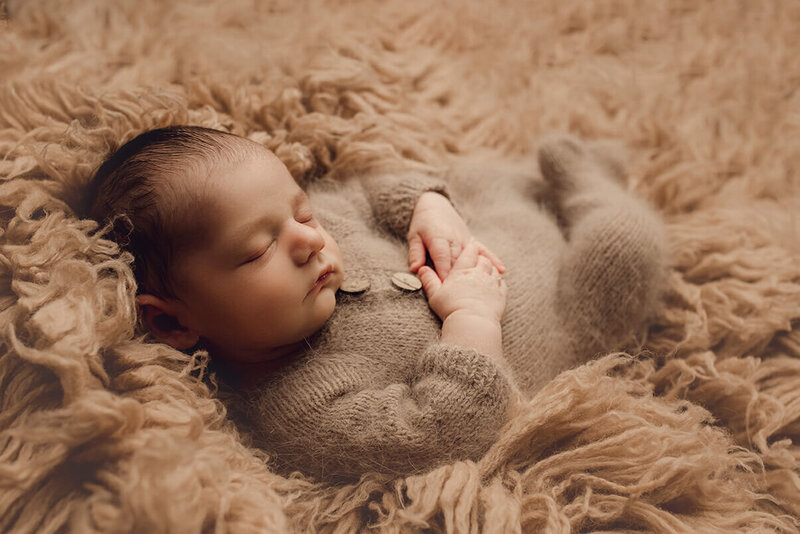 a sleeping newborn wearing a brown knitted romper on a brown fluffy rug