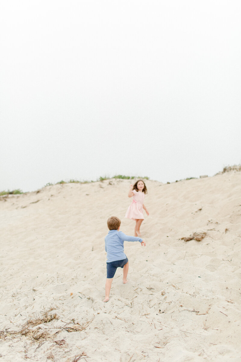 A young brother and sister climbing a sandy hill during photo session with Cape Cod photographer, Corinne Isabelle